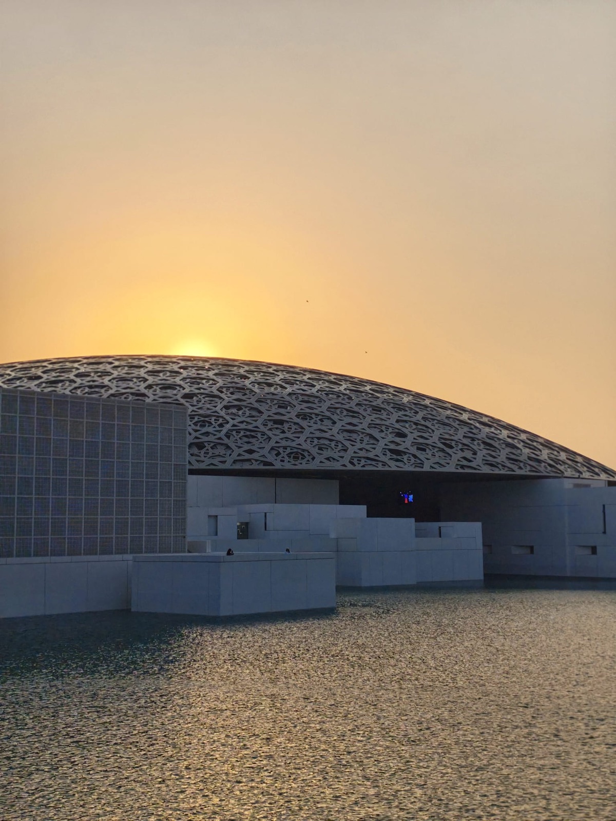 Die Kuppel des Louvre Abu Dhabi bei Sonnenuntergang über dem Wasser