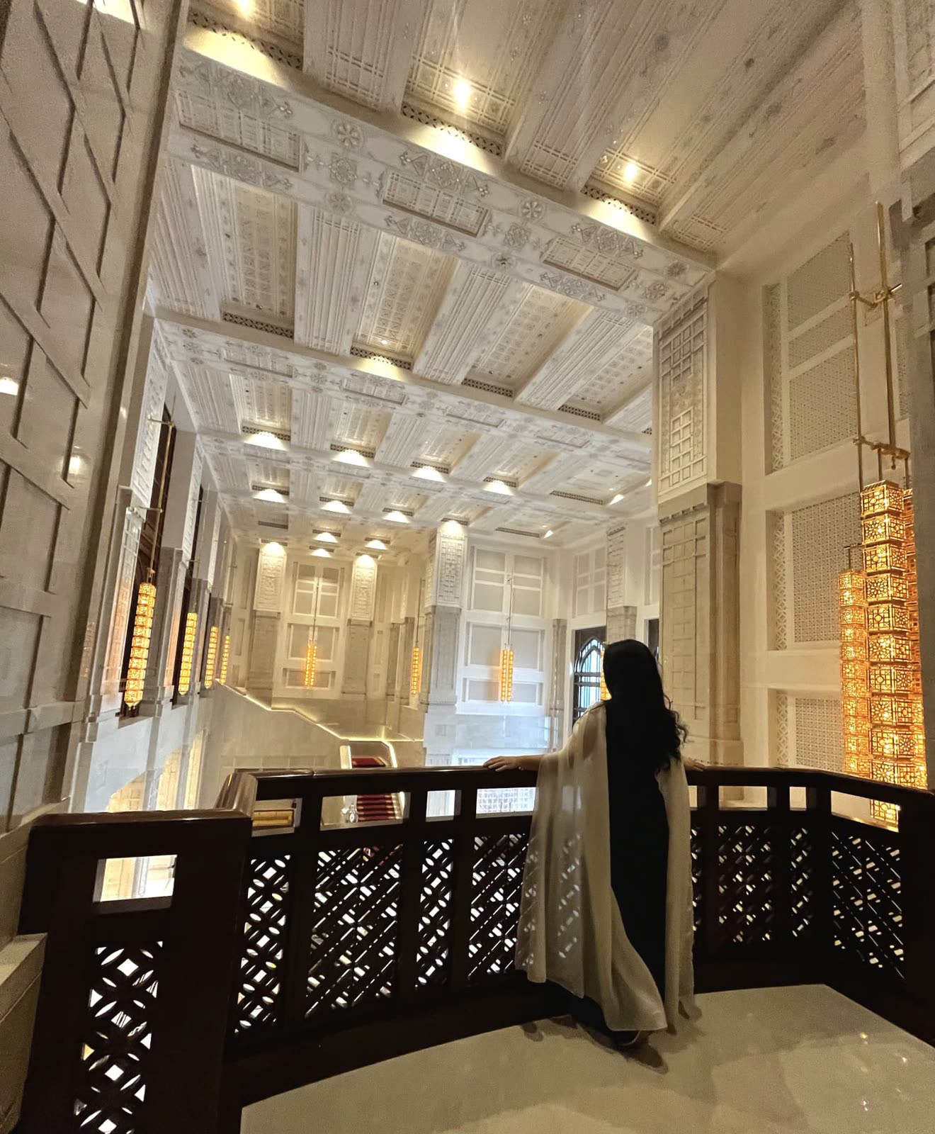 Reisende auf der Galerie einer prachtvollen Hotellobby mit goldenen Laternen